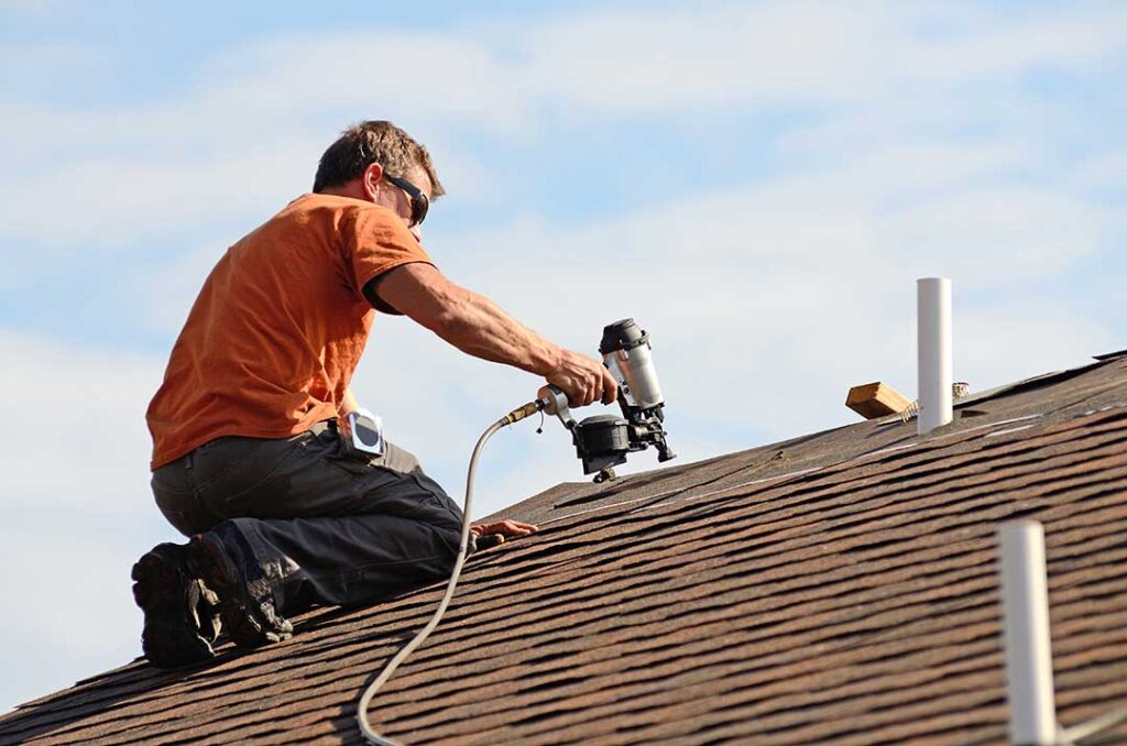 A homeowner using binoculars to inspect a shingled roof with dark streaks and green patches.