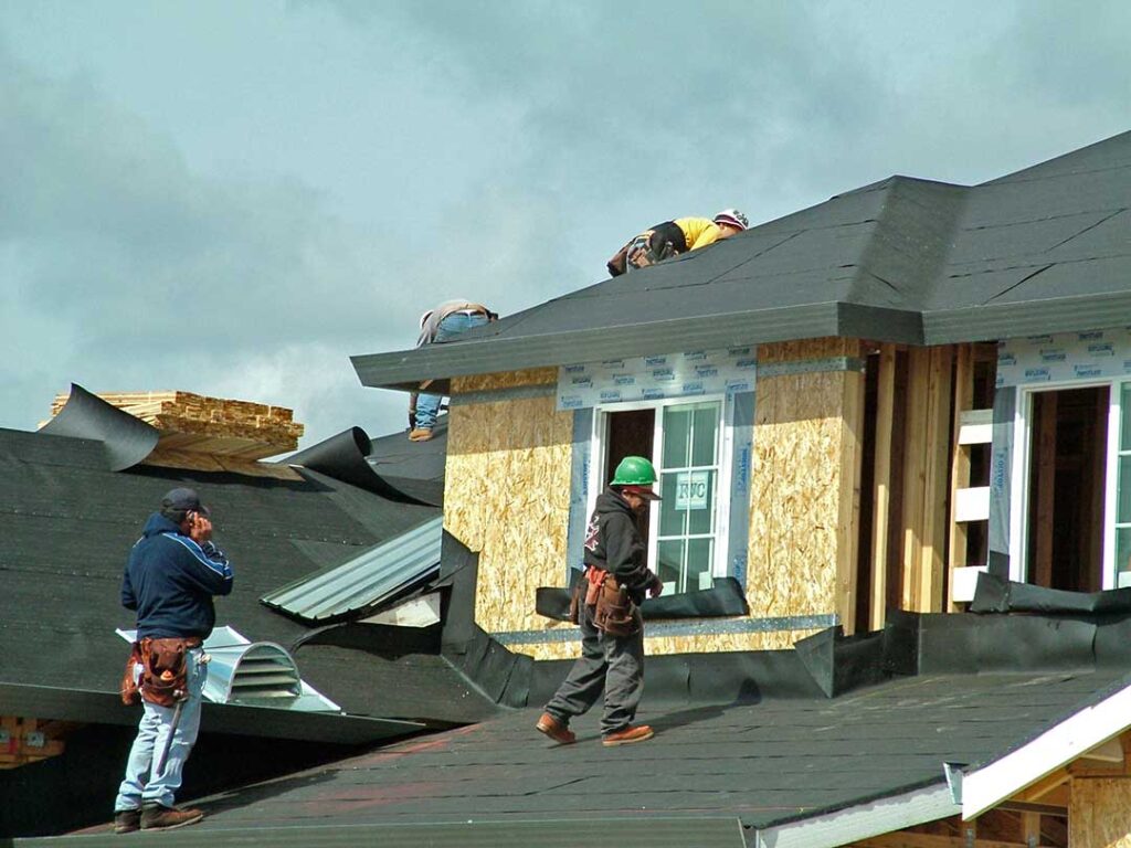 A close-up of an aging asphalt shingle roof with missing and curling shingles under cloudy sky.