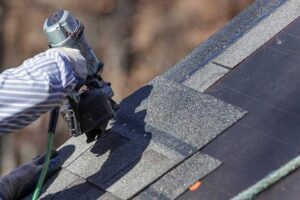 A worker installs new roof insulation in a residential attic with exposed rafters and blown-in insulation.