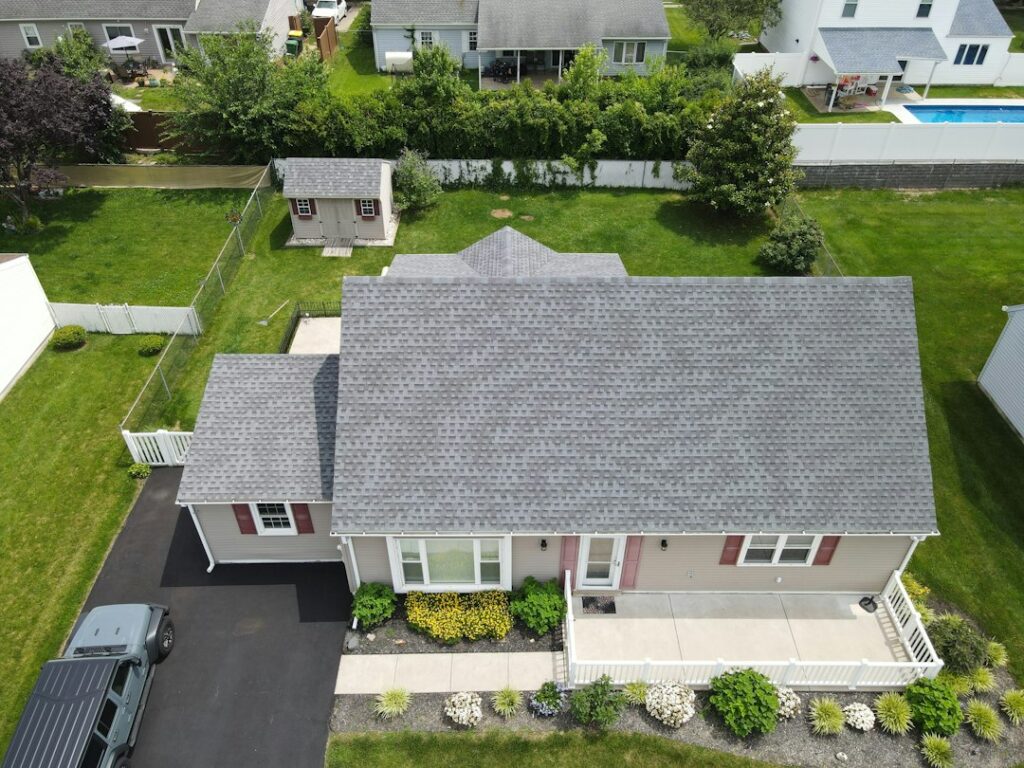 Roof color samples are held beside home siding and brick to compare how different shades look in natural light.