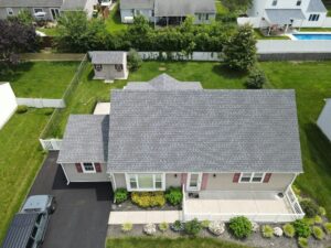 Roof color samples are held beside home siding and brick to compare how different shades look in natural light.