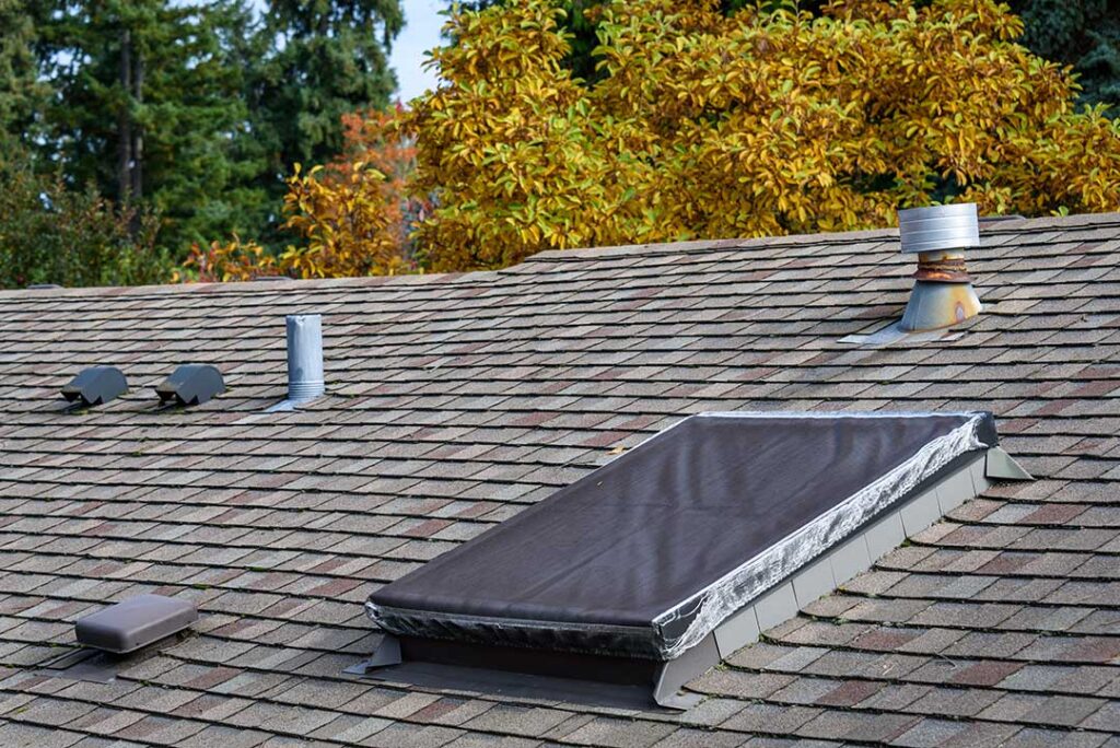 A person measures roof pitch with a level and tape measure beside a residential attic opening.